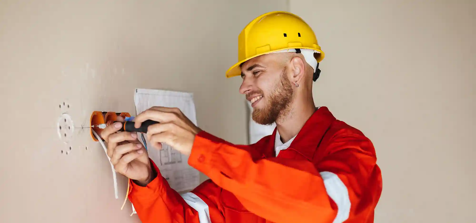 service_0003_smiling-foreman-orange-work-clothes-yellow-hardhat-using-screwdriver-repair-flat